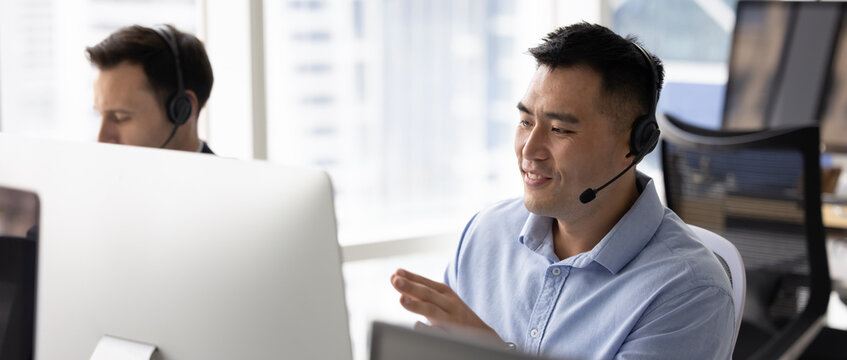 Customer service department. Wide panoramic image confident young man hotline operator helpdesk technician in headset contact client with friendly smile give live assistance support by computer screen