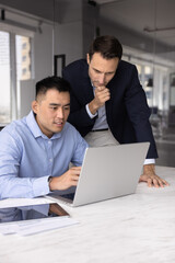 Fototapeta premium Collaborative brainstorming. Focused mid aged team leader project coordinator ceo examine notebook screen with intern colleague partner assist understanding work supervise task of younger professional