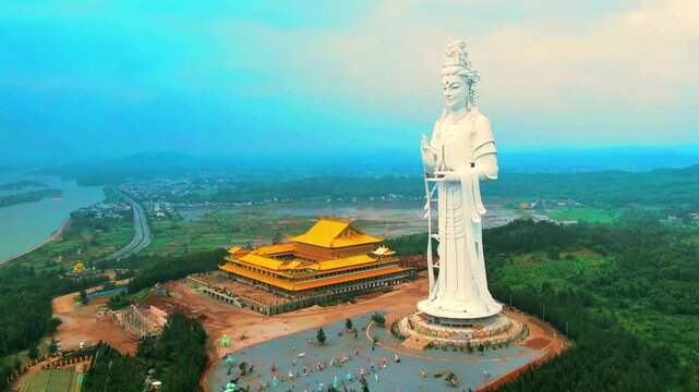 4K drone orbit focusing on the side profile of the towering Buddha statue and the adjacent traditional temple buildings on the hill.