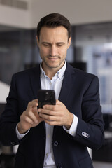 Obraz premium Confident adult man corporate manager executive messaging on cellphone in work office making online payment via mobile banking app managing digital document in corporate network reading business news