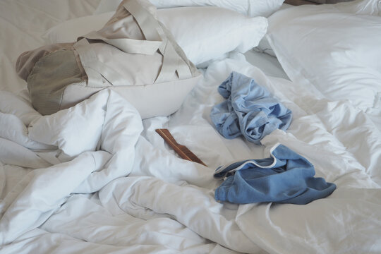 Clothes and bag on messy bed with white sheets