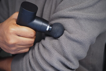 Naklejka premium Hand using massage gun on elbow for muscle relief
