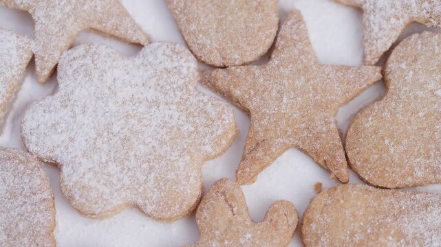 Homemade cookies dusted powdered sugar, assortment of star heart flower shapes on white surface closeup warm rustic tones crisp edges delicate texture cozy holiday baking mood