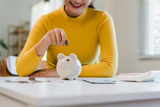 Happy young asian woman holding coin dropping into piggy bank concept for saving money finance budget and future investment plan