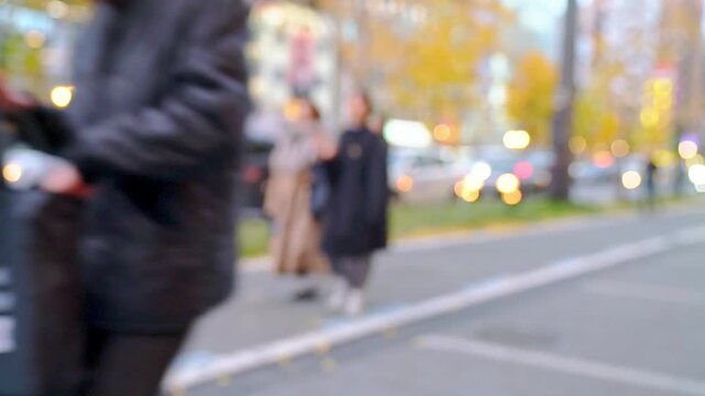 Out of focus bokeh background of a busy city street in autumn with cars, pedestrians and yellow trees. Soft urban traffic scene with golden fall colors and lights in an outdoor city setting.