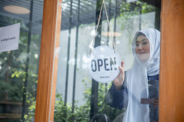 Obraz premium Muslim woman hanging open sign on cafe door preparing to welcome customers in the morning