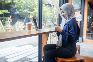 Fototapeta premium Muslim woman using tablet and laptop while working at cafe table with coffee cup