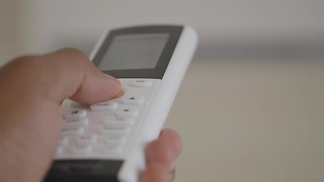 Close-up shot of a person using a remote control to adjust air conditioner settings, highlighting the power button and temperature controls with deliberate finger presses