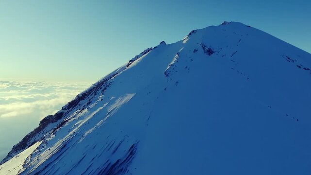 4K aerial drone view of the snow covered summit of Pico de Orizaba, also known as Citlaltepetl, the highest volcano in Mexico. Dramatic volcanic peak rising above a sea of clouds.