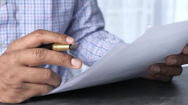 Close-up of hands holding pen and paper, reviewing document with thoughtful consideration, reviewing information