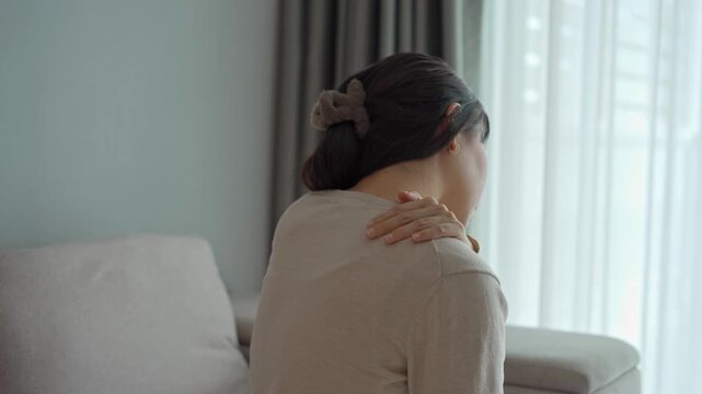 Woman suffering from neck pain while sitting on the couch at home, Health care and medical concept
