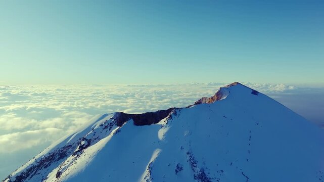 4K aerial drone view of the snow covered summit of Pico de Orizaba, also known as Citlaltepetl, the highest volcano in Mexico. Dramatic volcanic peak rising above a sea of clouds.