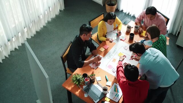 Top down view of diverse people brainstorming and making scrum task board. Group of skilled business team working together and writing sticky notes to share plan and using kanban board. Convocation.