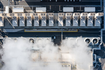 Aerial drone view of large data center cooling systems with industrial fans and steam rising from...