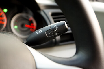 Close-up of a car turn signal and headlight control stalk behind the steering wheel, showing lighting and indicator controls used for vehicle operation and road safety. © AgFang