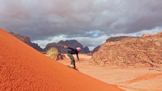 Beginner caucasian male sandboarder successfully sandboarding down steep red dune in Wadi rum showing skill balance confidence achievement and adventure Jordan