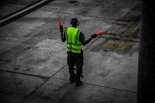 Airport marshaller in high-visibility vest directing aircraft with illuminated wands on tarmac