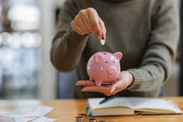 A woman adds coins to a charming pink piggy bank, symbolizing the importance of saving money and...
