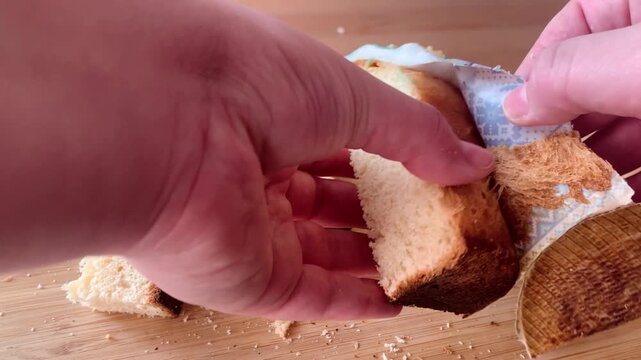 Female hands breaking and cutting traditional Easter bread. Fresh homemade kulich with soft texture inside. Easter baking and festive pastry.
