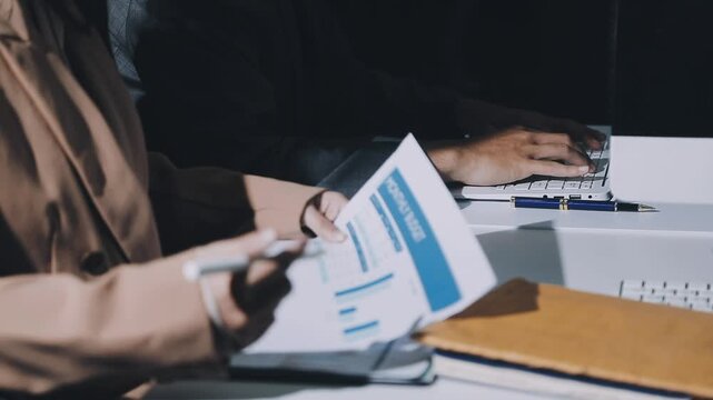 Accountant reviewing printed financial reports at messy office desk with calculator and sticky notes under soft window daylight for audit and corporate finance work