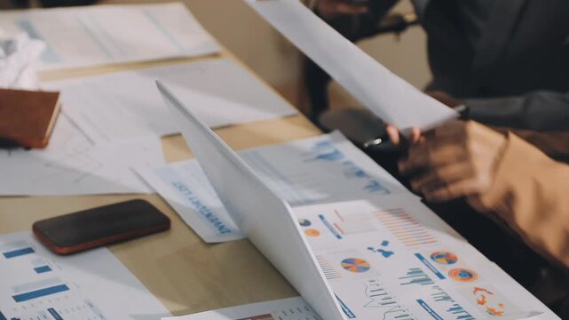 Accountant reviewing printed financial reports at messy office desk with calculator and sticky notes under soft window daylight for audit and corporate finance work