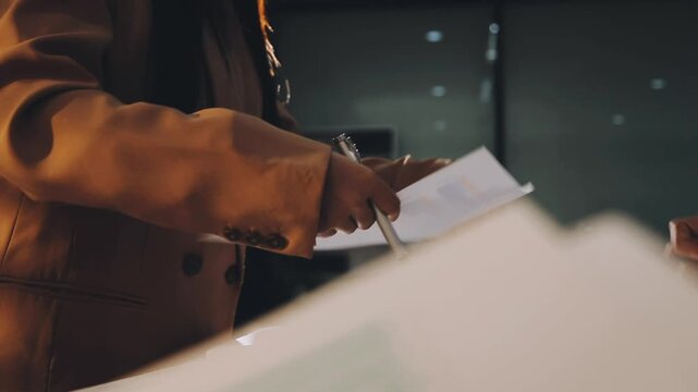 Accountant reviewing printed financial reports at messy office desk with calculator and sticky notes under soft window daylight for audit and corporate finance work