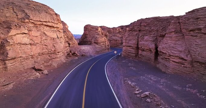 Aerial view of winding asphalt road through rock canyon at dusk, Xinjiang, China. 