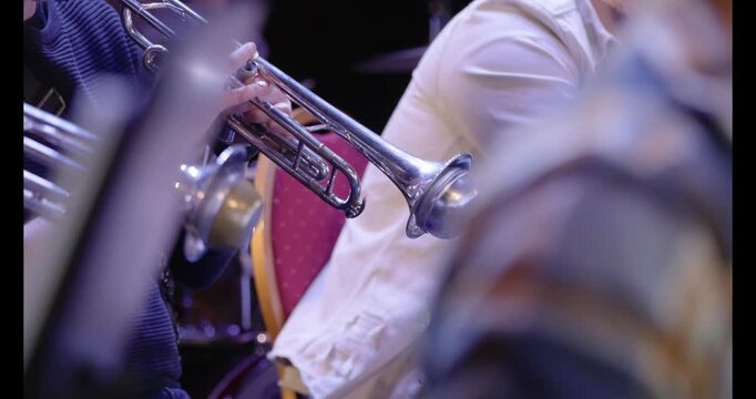 A slow motion video of musicians playing trumpets with straight mutes during a wind ensemble rehearsal in preperation for a concert