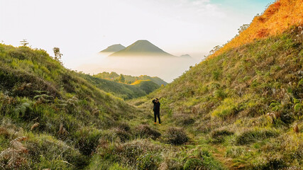 Full Body View of Male Hiker Standing in Lush Valley of Mount Prau with Misty Peak Background