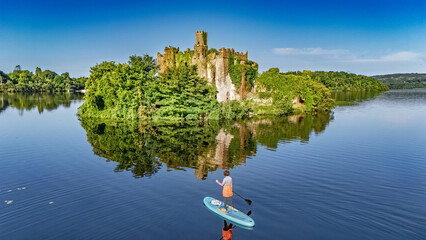 Aerial drone view of woman paddling SUP board on beautiful Lough Key lake with McDermotts Castle on small island, stand up paddling water adventure on vacation, travel in Ireland