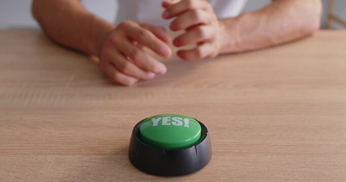 On a wooden desk, hand presses green yes button to signal approval, confirm intent, and finalize a choice or decision. A hand presses a green yes button. Concept of pressing, accept and solution.