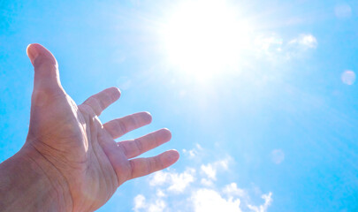 Hand reaching for the sun against a bright blue sky. It evokes feelings of freedom and connection with nature