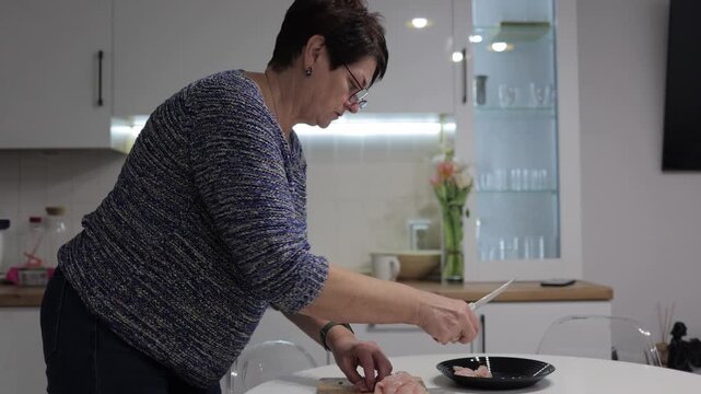 Woman cutting chicken breast on wooden board