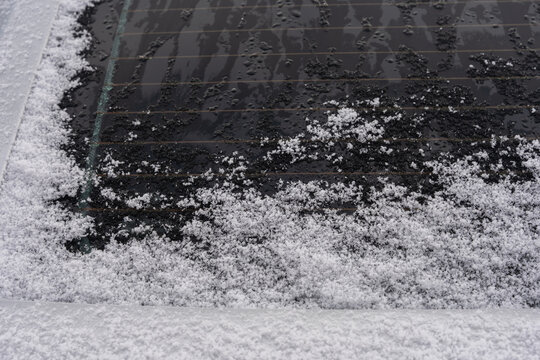 Rear window defroster melting snow on heated glass shows clear heating lines and water droplets. Visible defrost grid warms the car rear window and creates streaks and texture on winter surface