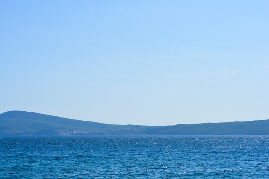 A wide coastal view from Selce across the blue Adriatic Sea toward the distant hills of Krk Island and the historic town of Vrbnik.