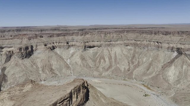 Drone flies over cliff above dried up riverbend at Fish River Canyon in the Namib Desert, Namibia in the late morning