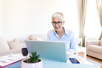 Mature businesswoman working on laptop at home office. Senior female professional using computer...