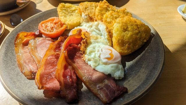 Traditional English fry fried breakfast with hash browns, eggs, bacon and tomato