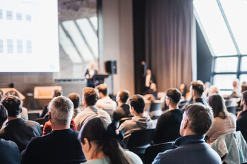 Female speaker giving a talk on corporate business conference. Unrecognizable people in audience at...