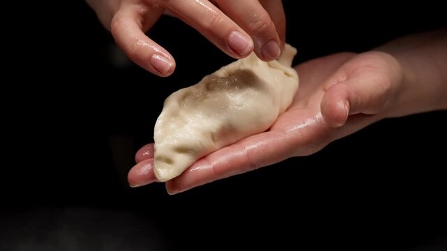 Close-up sequence of hands carefully folding and sealing a fresh dumpling against a dark background, highlighting delicate finger movements and smooth dough texture