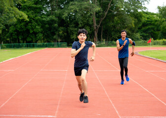 Obraz premium Two young male athletes running on stadium track during outdoor training. Fitness runners sprinting together on running track in sports field. Healthy lifestyle and endurance workout concept