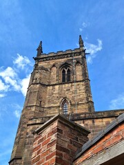 Fototapeta premium The tower of St Mary de Castro Church in Leicester, rises in warm sandstone against clear blue sky. Gothic arched windows, battlements, and carved stone detailing define the medieval structure.