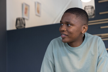 African American man sitting, turning left in home lounge wearing sage crewneck and hoop earring © wavebreak3