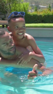 Child climbing onto father's back starting father paddling, holding and sharing playful pool bond