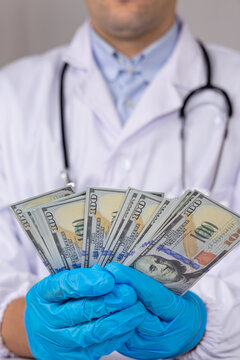 Un m&eacute;decin en blouse blanche et st&eacute;thoscope, avec des gants en nitrile bleu, qui tient des billets de banque dans ses mains, signifiant les frais m&eacute;dicaux. Le format est vertical.