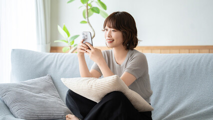 ソファでくつろぎながらスマートフォンを見る女性, Woman relaxing on a sofa while using a smartphone © Trickster*