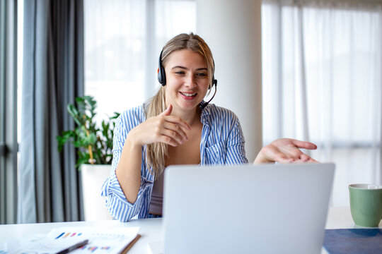 Happy woman wearing headset during video call on laptop. Customer support, remote work and online communication concept. Friendly female operator or student talking and gesturing during webinar.