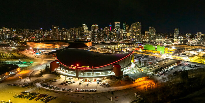 Calgary, Alberta, Canada. March 8, 2026. Wide-angle aerial view of the Scotiabank Saddledome and BMO Centre at night with the city skyline illuminated.