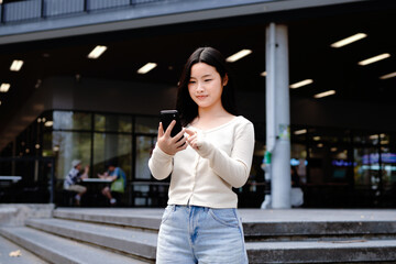 Fototapeta premium asian woman college student holding and looking smartphone walking in campus