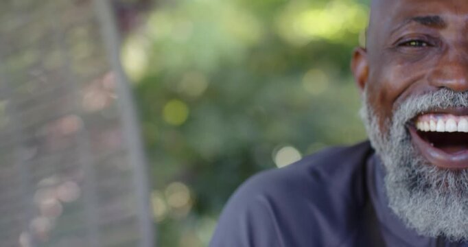 Mature man reacting to off-camera joke, laughing sitting on porch with woven backrest and grey tee